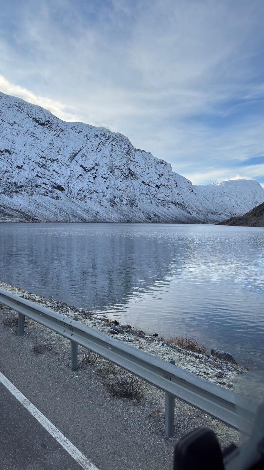Zasněžená skála nad klidnou hladinou norského jezera
