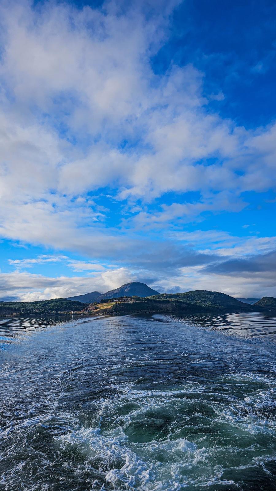 Norský fjord s horami a stopou za trajektem