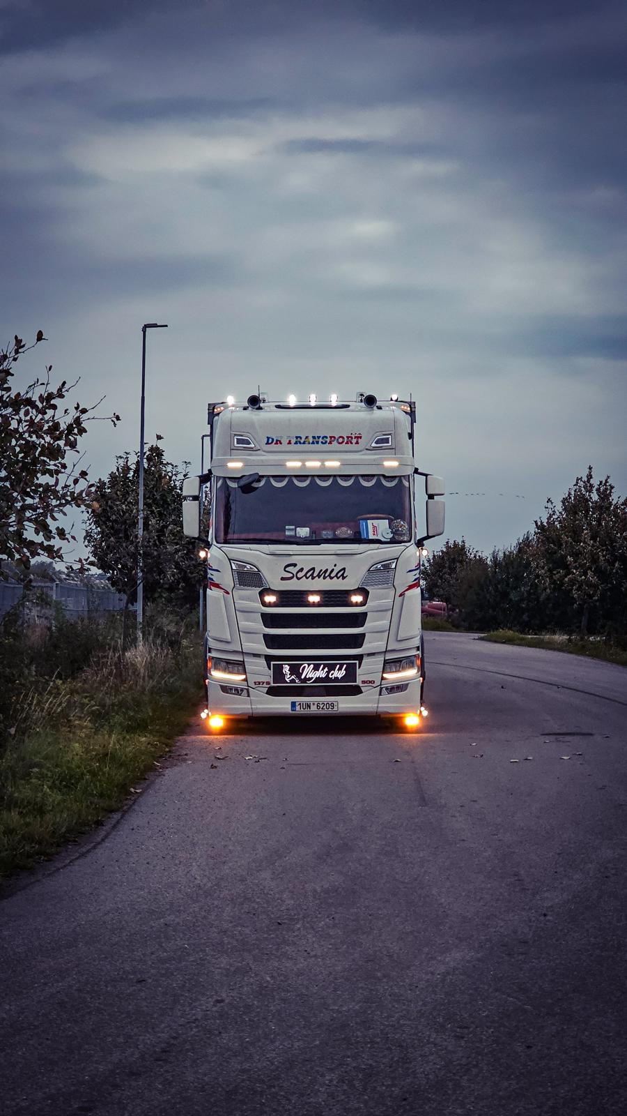 Scania Night Club DK Transport s rozsvícenými světly za soumraku