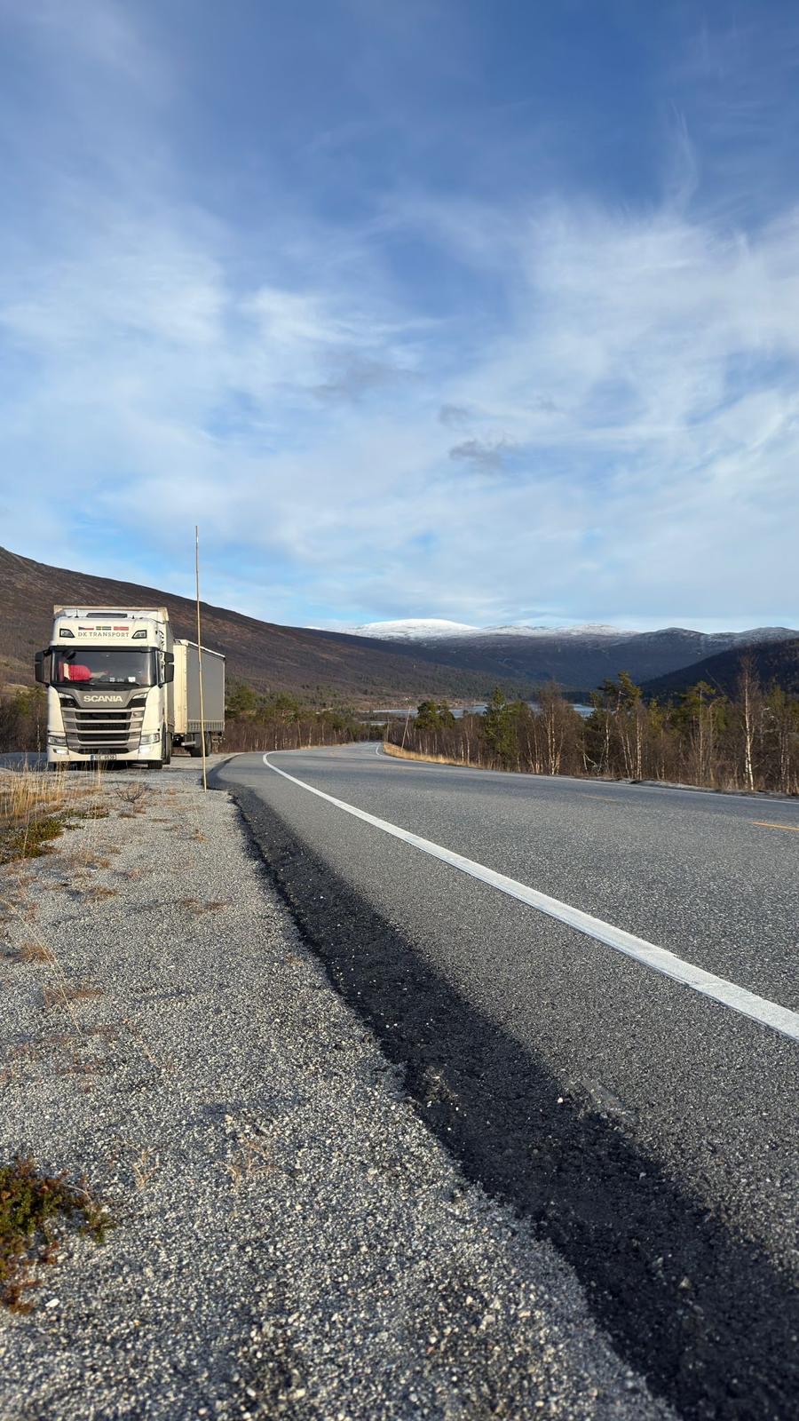 Scania DK Transport zaparkovaná u norské silnice s výhledem na zasněžené hory