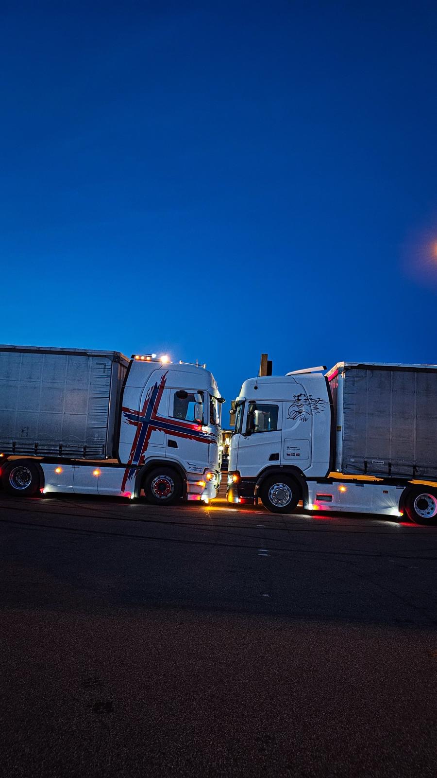 Dvě Scanie DK Transport stojící proti sobě za soumraku